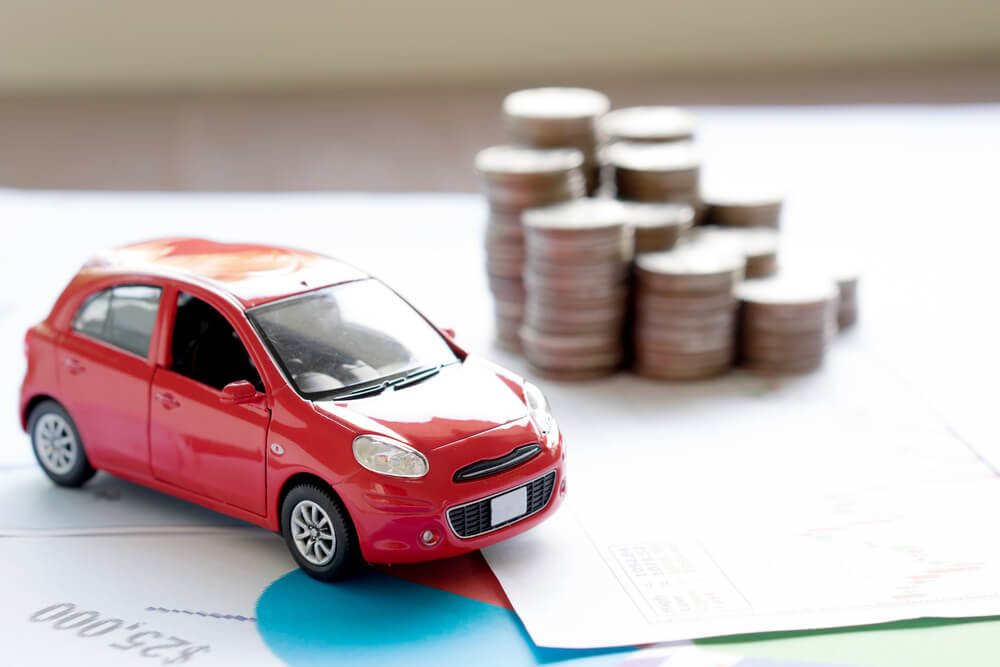 miniatura de carro vermelho ao lado de moedas, representando o custo do km rodado para carros de passeio.